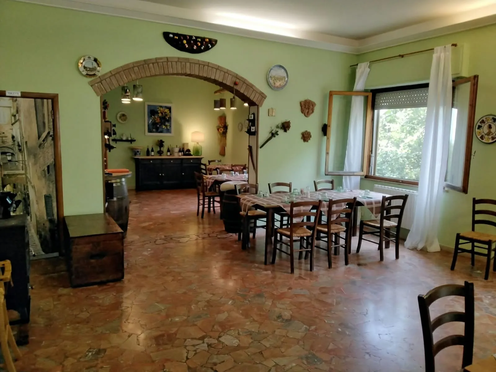 La sala dell'osteria: pareti verdi, un arco in mattoni, pavimento in cotto e i tavoli apparecchiati.
